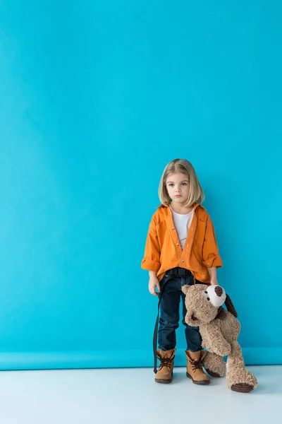 Grave et adorable enfant tenant ours en peluche sur fond bleu — Photo de stock
