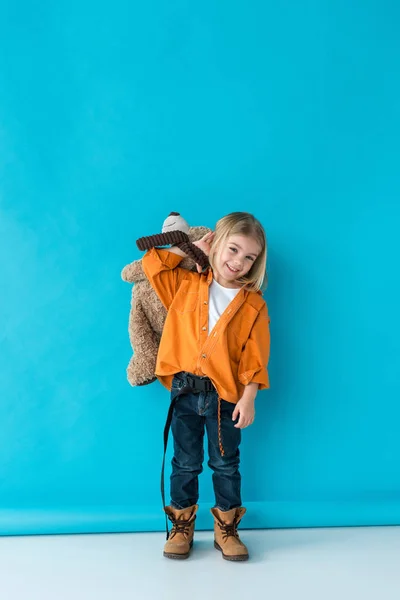 Smiling and cute kid holding teddy bear on blue background — Stock Photo