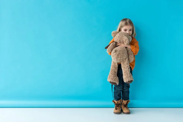 Мила і чарівна дитина тримає плюшевого ведмедя на синьому фоні — стокове фото