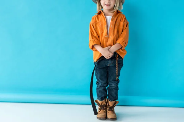 Vue recadrée de l'enfant en jeans et chemise orange sur fond bleu — Photo de stock