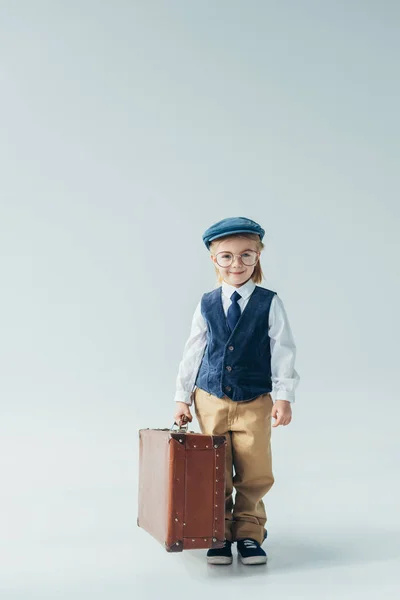Happy kid in retro vest and cap holding suitcase and looking at camera — Stock Photo