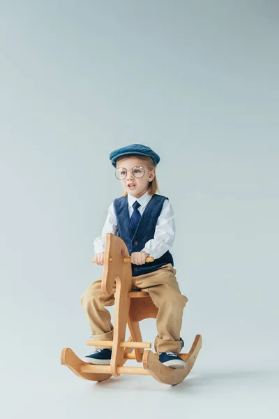 Enfant en gilet rétro et casquette à cheval à bascule sur fond gris — Photo de stock