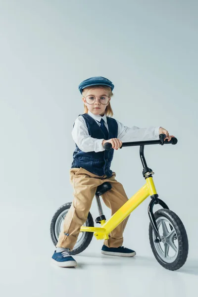 Enfant en gilet rétro et casquette vélo d'équitation et regardant la caméra sur fond gris — Photo de stock