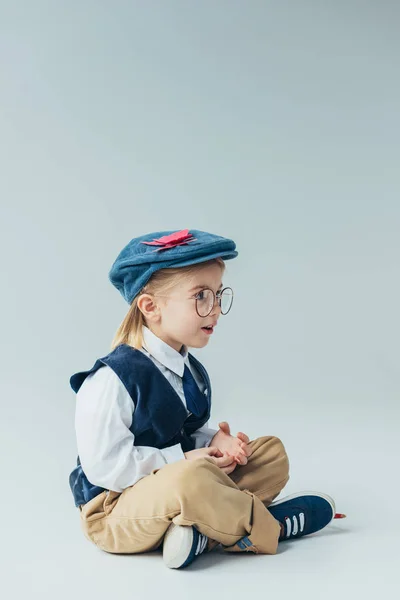 Überraschtes Kind sitzt mit überkreuzten Beinen auf dem Boden und schaut weg — Stockfoto