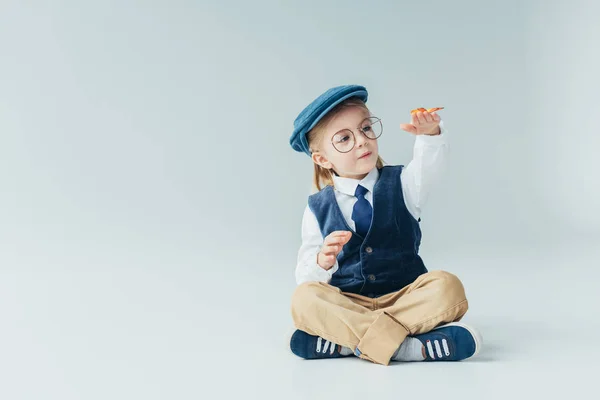 Adorable kid sitting on floor with crossed legs and holding butterfly on grey background — Stock Photo