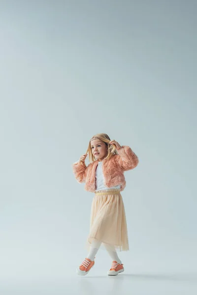 Cute kid in faux fur coat and skirt walking and looking away isolated on grey — Stock Photo