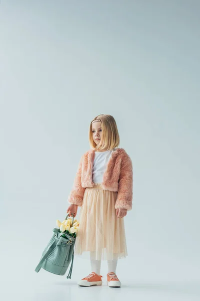 Cute kid holding bag with white tulips and looking away isolated on grey — Stock Photo