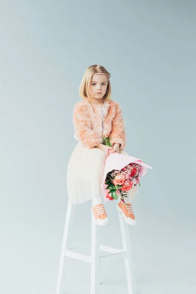 Pensive kid in faux fur coat and skirt sitting on highchair and holding bouquet — Stock Photo