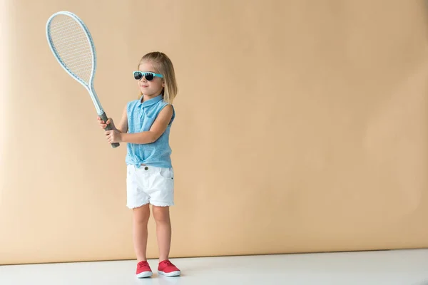 Cute kid in shirt and shorts playing with racket on beige background — Stock Photo