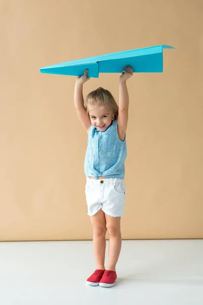 Criança adorável e sorridente em camisa e shorts segurando avião de papel azul — Fotografia de Stock