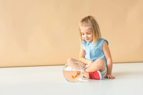 Carino bambino seduto con le gambe incrociate e guardando boccia di pesce — Foto stock