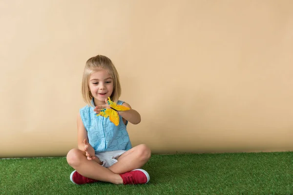 Счастливый и симпатичный ребенок, сидящий со скрещенными ногами и держащий бабочку — стоковое фото