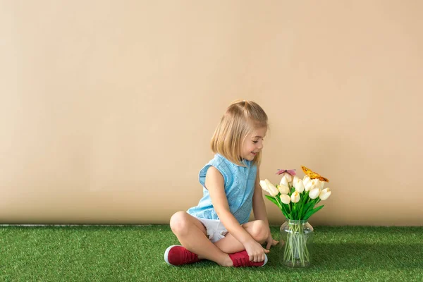 Happy child sitting with crossed legs and looking at flowers and butterflies — Stock Photo