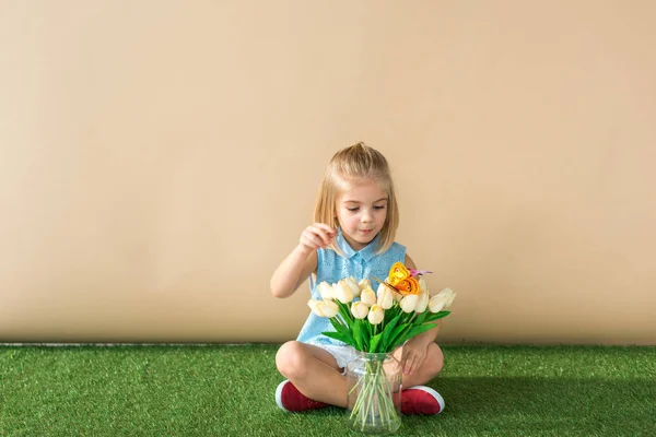 Child sitting with crossed legs, looking at flowers and catching butterfly — Stock Photo