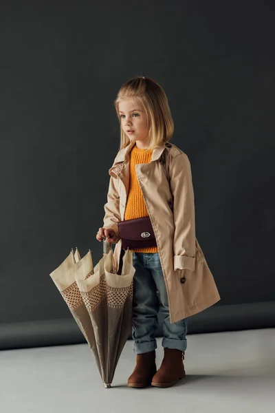 Enfant rêveur en trench coat et jeans tenant parapluie et détournant les yeux — Photo de stock