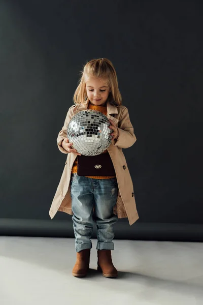 Niño feliz en gabardina sosteniendo bola disco sobre fondo negro - foto de stock