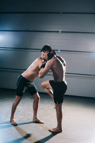 Muscular barefoot mma fighter kicking sportive opponent with knee — Stock Photo