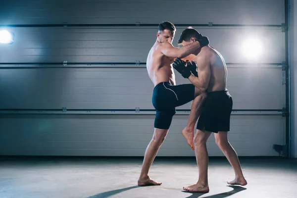 Vue latérale du combattant mma musclé donnant des coups de pied à l'adversaire sportif dans l'estomac avec genou — Photo de stock