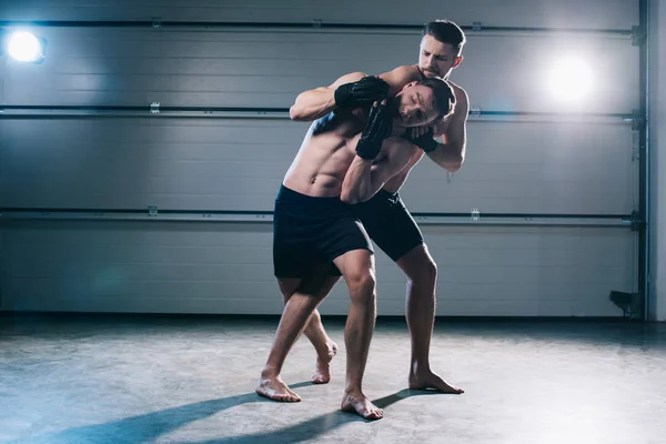 Muscular mma fighter doing chokehold to sportive shirtless opponent — Stock Photo