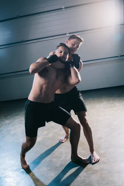 Barefoot muscular mma fighter doing chokehold to sportive shirtless opponent — Stock Photo