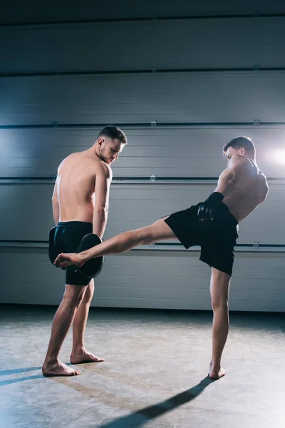 Strong muscular shirtless mma fighter practicing low kick with another sportsman — Stock Photo
