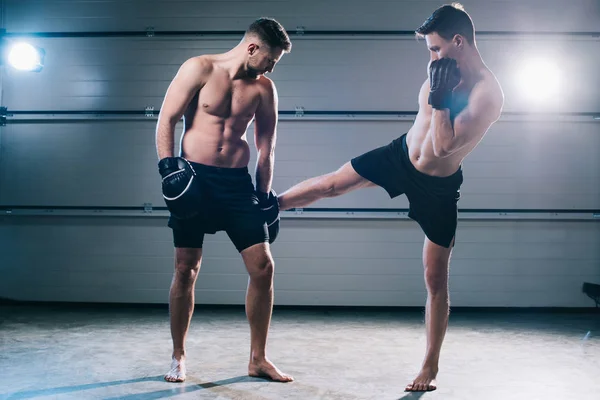 Strong muscular barefoot mma fighter practicing low kick with another sportsman — Stock Photo