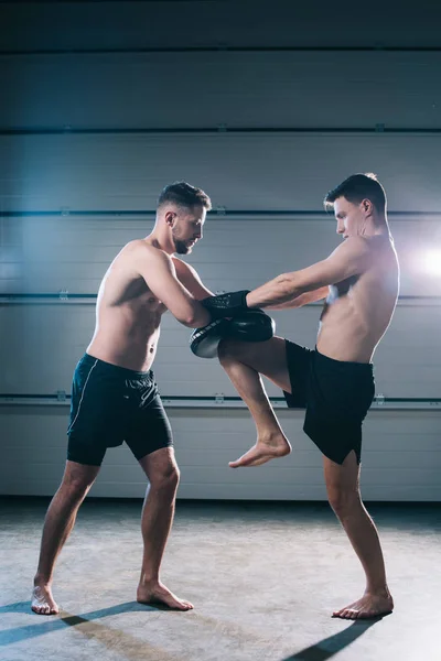 Athletic muscular barefoot mma fighter practicing kick with another sportsman during training — Stock Photo