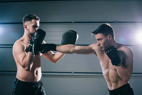 Athletic muscular shirtless mma fighter practicing punch with another sportsman during training — Stock Photo