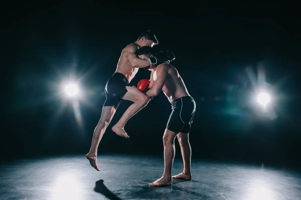Shirtless muscular mma fighter in boxing gloves kicking another with knee — Stock Photo