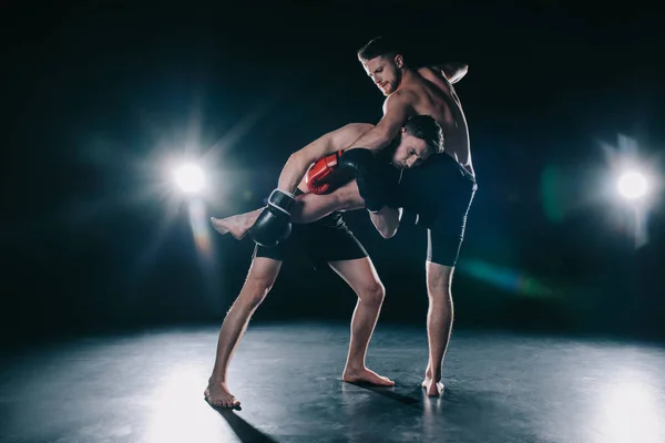 Barefoot strong muscular mma fighter in boxing gloves clinching another while sportsman kicking him — Stock Photo