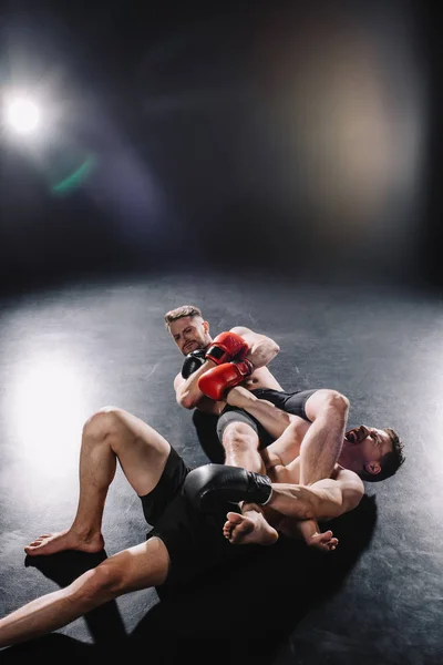 Strong shirtless mma fighter doing painful joint lock to another sportsman while man screaming on floor — Stock Photo