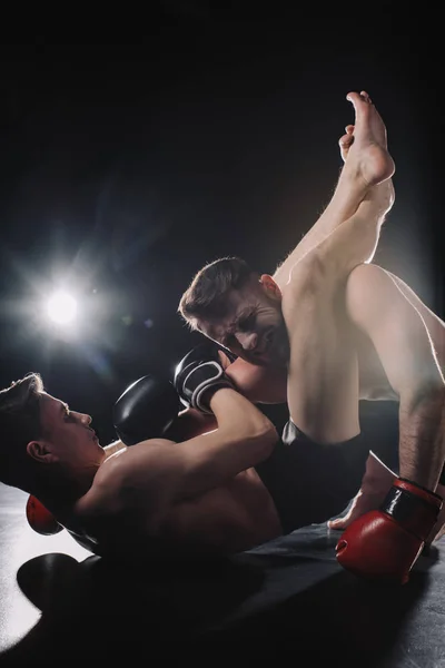 Strong shirtless mma fighter doing painful joint lock with legs to another sportsman on floor — Stock Photo