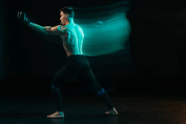 Larga exposición de deportista muscular mma fighter haciendo ponche en luz verde sobre negro - foto de stock