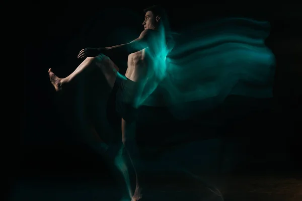 Long exposure of shirtless muscular mma fighter doing kick in green light on black — Stock Photo