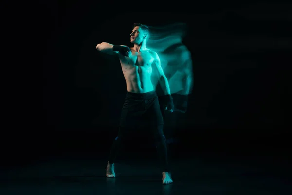 Long exposure of shirtless muscular sportsman in stance in green light on black — Stock Photo