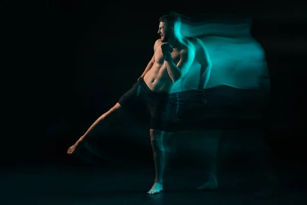 Long exposure of green light and sporty muscular mma fighter doing kick and looking away — Stock Photo