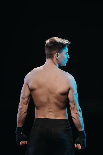 Vista posterior de deportista musculoso en vendajes y luz azul aislado en negro - foto de stock
