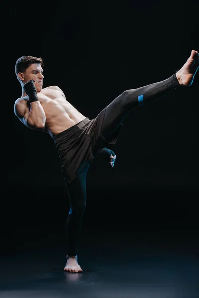 Muscular shirtless and barefoot mma fighter in bandages doing kick — Stock Photo