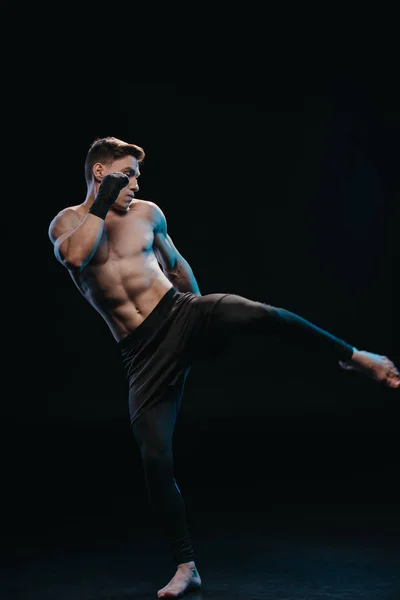 Muscular shirtless and barefoot mma fighter in bandages doing kick isolated on black — Stock Photo