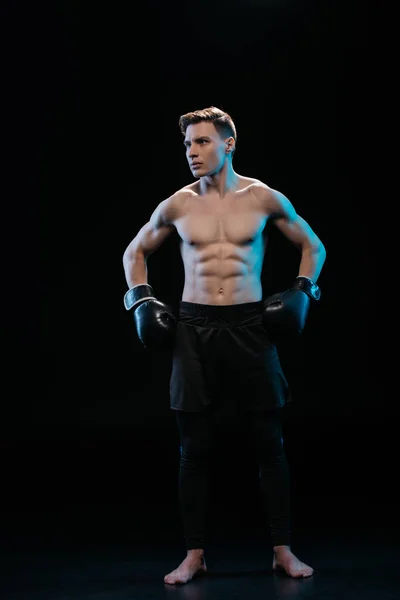 Confiado boxeador deportivo muscular en guantes de boxeo posando en negro - foto de stock