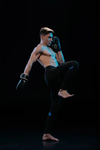 Confiante muscular descalço mma lutador em luvas de boxe fazendo chute no preto — Fotografia de Stock