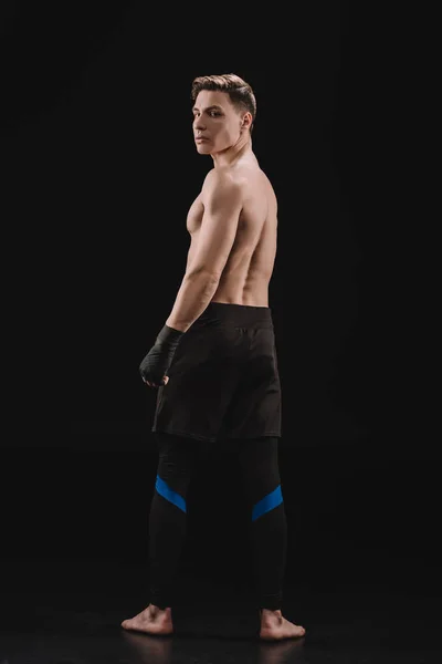 Rückansicht einer starken, barfüßigen, muskulösen MMA-Kämpferin, die auf schwarz in die Kamera blickt — Stockfoto