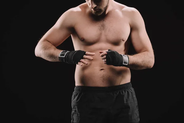 Partial view of muscular sportsman looking at hands with bandages isolated on black — Stock Photo