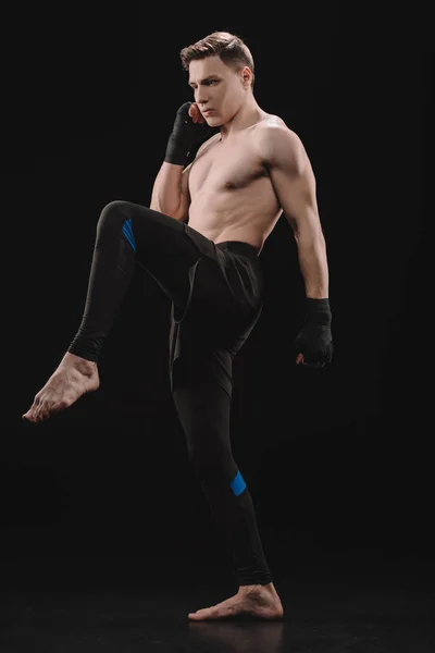 Сильный мускулистый босиком спортсмен в бинтах делает удар на черный — стоковое фото