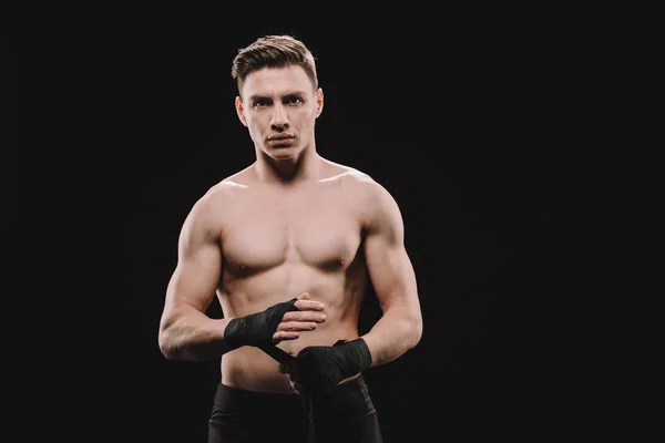 Strong shirtless muscular mma fighter fixing bandages and looking at camera isolated on black — Stock Photo