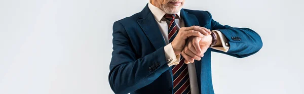 Панорамний знімок зрілих бізнесмена в костюмі, дивлячись на годинник, ізольовані на сірому — стокове фото