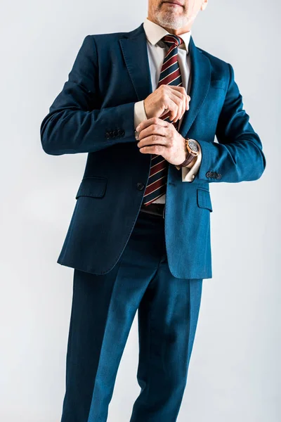 Abgeschnittene Ansicht eines reifen Geschäftsmannes, der Anzug anfasst, während er isoliert auf grau steht — Stockfoto