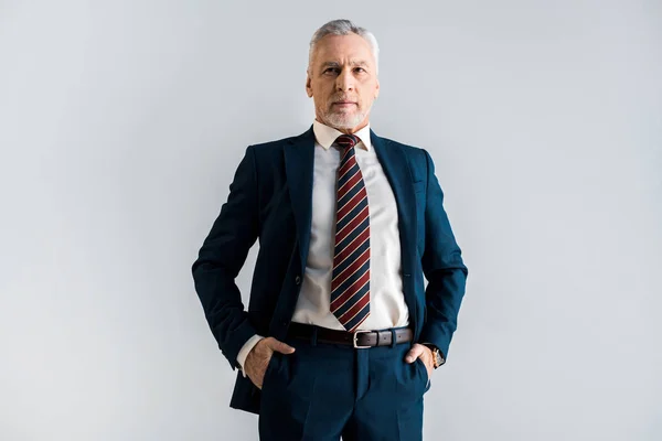 Ernstzunehmender Geschäftsmann steht mit Händen in Taschen isoliert auf grau — Stockfoto