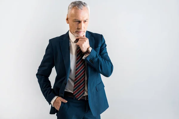 Pensive mature businessman in suit standing with hand in pocket isolated on grey — Stock Photo