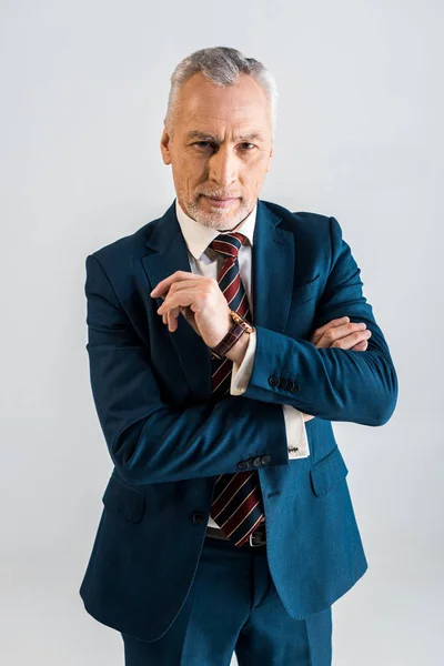 Pensive mature businessman in suit standing with crossed arms isolated on grey — Stock Photo